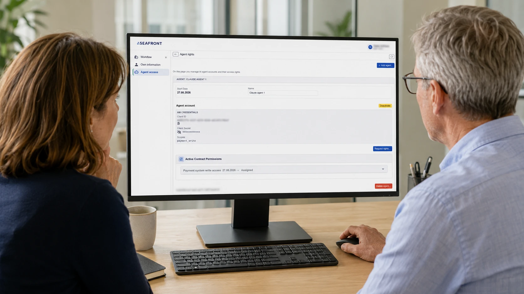 Two colleagues reviewing AI agent access rights at a desk: the Seafront interface shows the agent's account, credentials, scopes and active contract permissions, with options to request, deactivate or delete the agent.