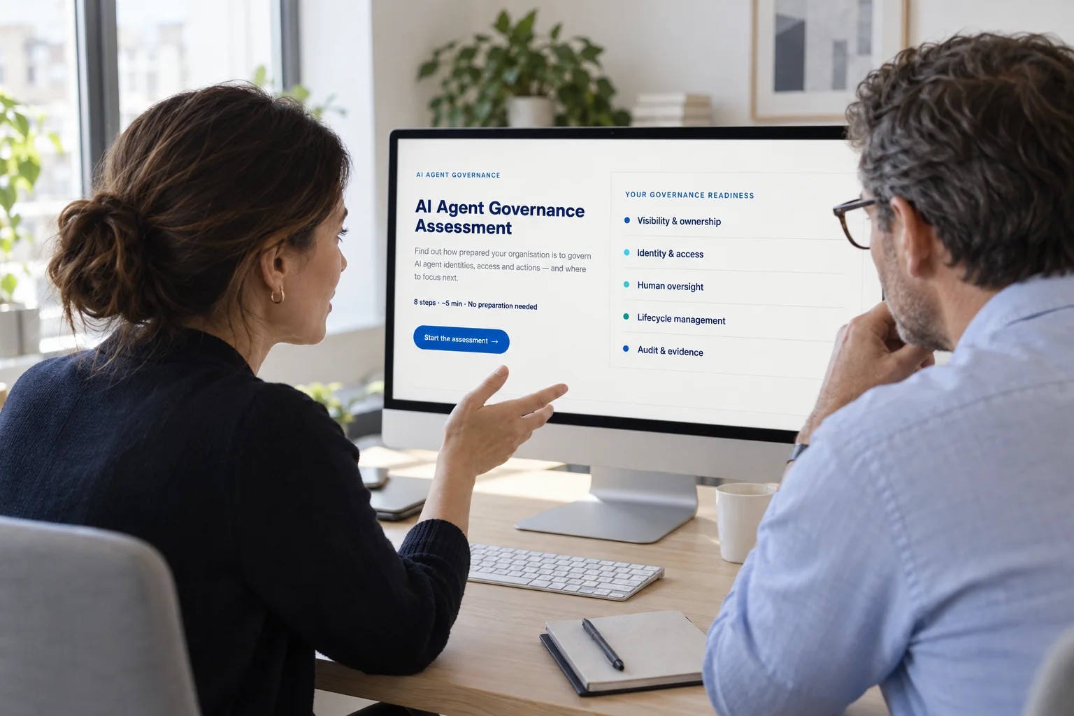 Two colleagues reviewing the AI Agent Governance Assessment on a desktop monitor.